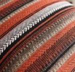 Gros plan sur le motif texturé d'une housse de coussin rayée, tons rouge et marron