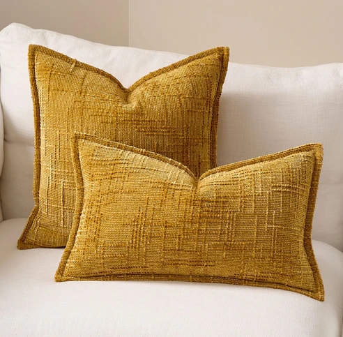 Deux coussins dorés Oro sur un canapé blanc, dont un coussin texturé rectangulaire et un carré